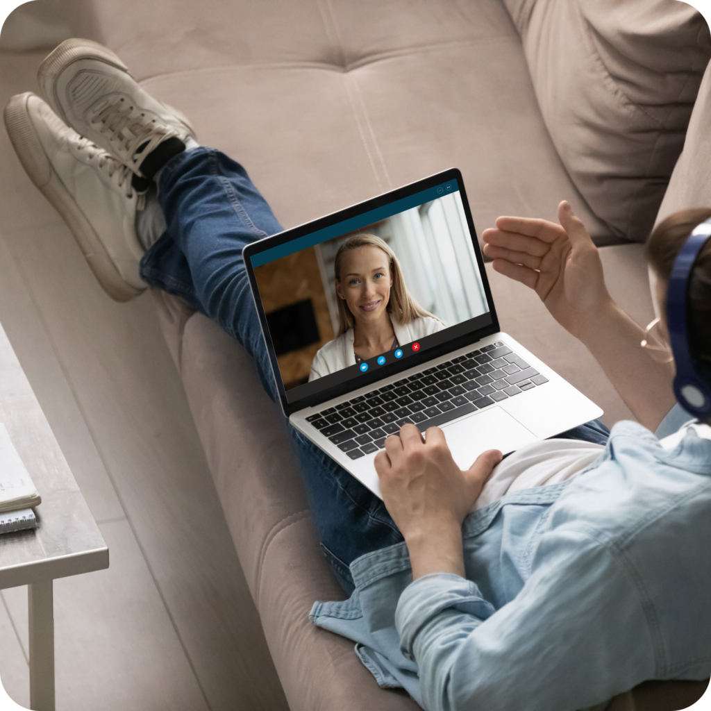 Young man stretched out on couch with laptop on his lap doing a video call with his dating coach