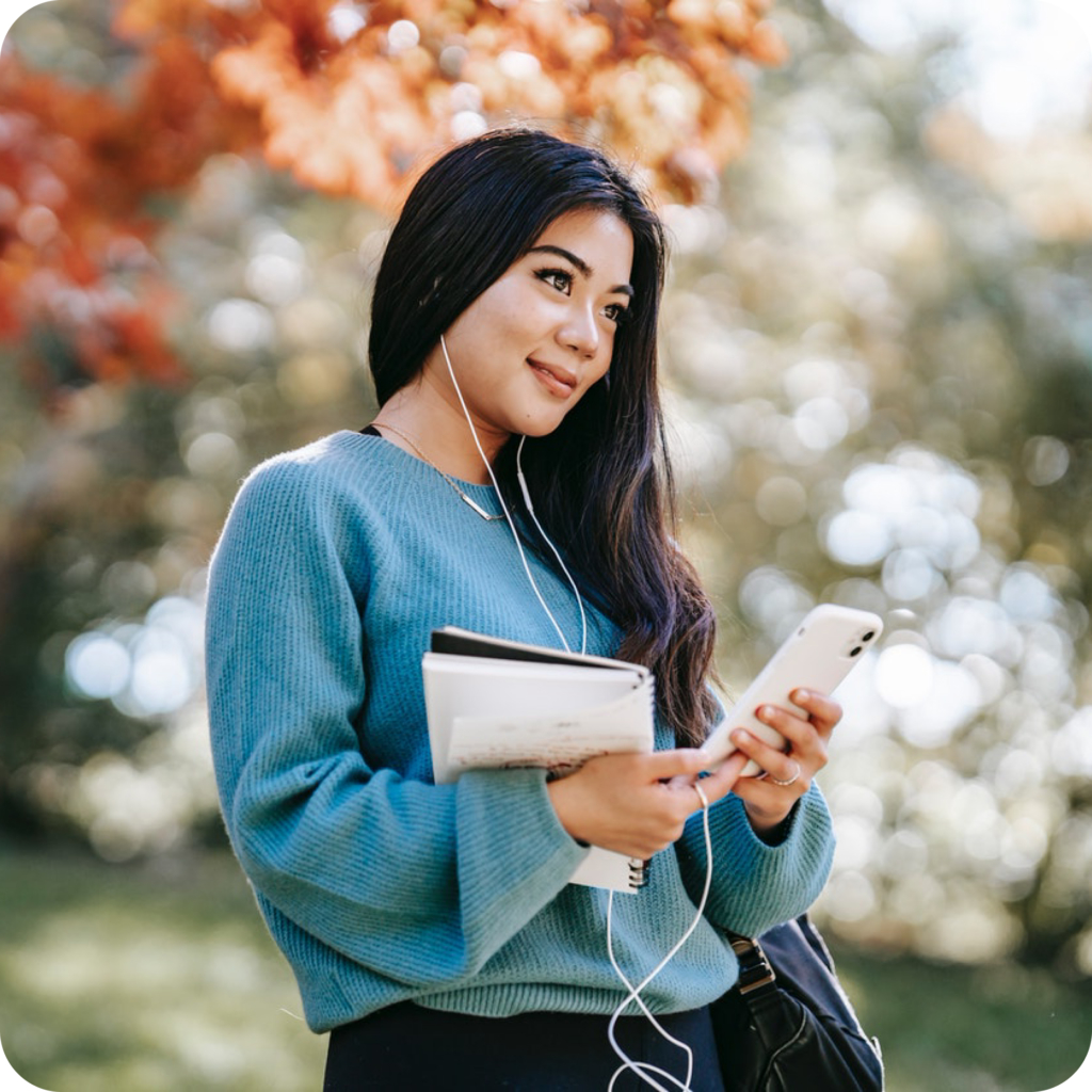 young asian woman with long dark hair wearing a blue sweater listening on ear phones to dating photographer on phone consultation.