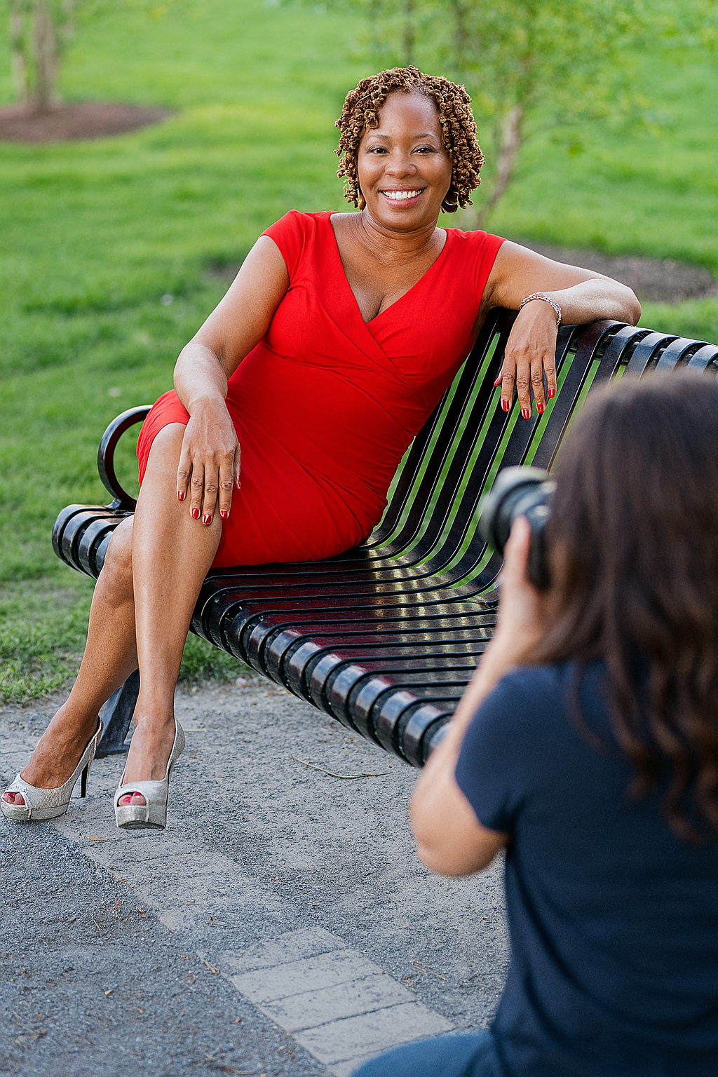 smiling black woman in sleeveless red dress sitting park bench being photographed for dating profile photo